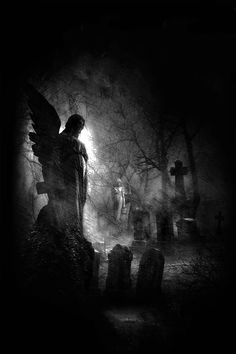 a black and white photo of an angel standing in front of tombstones at night