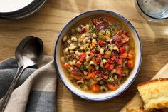 a bowl of soup with bread and spoons on the table next to it,