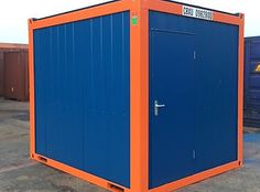 an orange and blue portable toilet sitting on top of a parking lot next to shipping containers