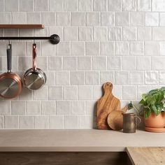 pots and pans are hanging on the wall above a counter with utensils