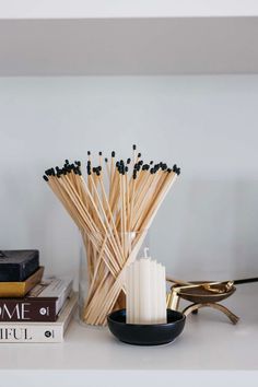 candles and books on a shelf in a room with white walls, black accents and gold accessories