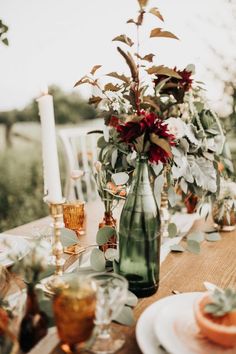 the table is set with plates, candles and vases filled with flowers on it