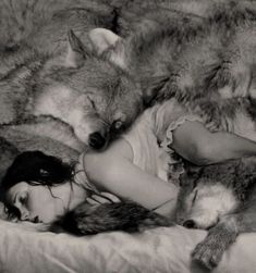 a black and white photo of a woman laying in bed with two grey wolfs