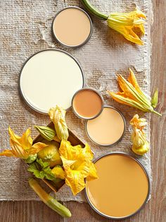 four different types of paint sitting on top of a wooden table next to yellow flowers