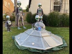 three silver alien statues sitting on top of a lush green field next to a house