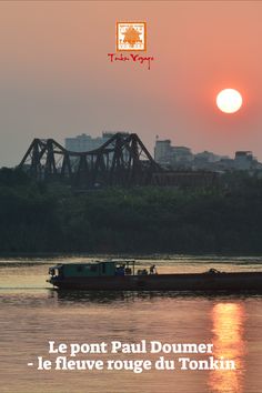 a boat floating on top of a river next to a bridge with the sun in the background