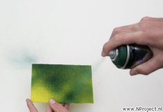 someone is painting the wall with green and yellow paint on it, while another hand holds a marker