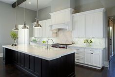 a large kitchen with white cabinets and marble counter tops, along with two pendant lights hanging from the ceiling