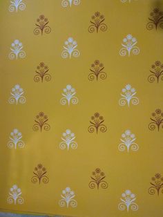 a yellow wall with white flowers and swirls on it, in front of a window