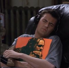 a man with headphones laying on top of a couch holding an orange book in his lap