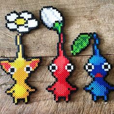 four pixelated pokemon brooches are sitting on a wooden surface, each with different colors and shapes