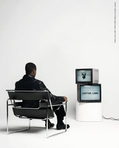 a man sitting in a chair next to two televisions with the same screen on them