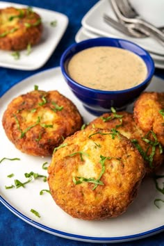 three crab cakes on a plate next to a bowl of dipping sauce and silverware