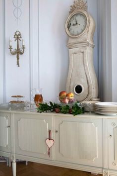 a white clock sitting on top of a cabinet next to plates and cups in front of it