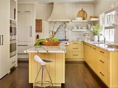 a kitchen with yellow cabinets and white counter tops, an island in the middle has a bowl of fruit on it