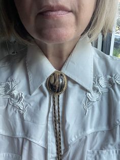 Step into the bold style of the 1980s with this Vintage Unisex Bolo Tie, a distinctive piece of vintage costume jewelry that captures the spirit of Western fashion. This versatile accessory features a classic bolo tie design, with intricately detailed tips and a stylish centerpiece that adds a touch of rugged elegance to any outfit. Bolo ties surged in popularity during the 1980s, becoming a fashion statement that transcended traditional Western wear and found its way into mainstream culture. Ce Vintage Lariat Bolo Ties For Rodeo, Vintage Gold Lariat Bolo Tie, Vintage Formal Bolo Tie Lariat, Adjustable Vintage Lariat Necklace, Vintage Adjustable Bolo Tie For Formal Occasions, Bolo Tie Outfit Women, Bolo Tie Women Outfit, Tie Women Outfit, Bolo Tie Women