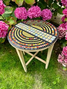 a mosaic table sitting in the grass next to some pink hydrangeas and purple flowers