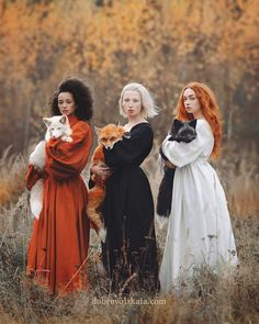 three women in long dresses are holding cats