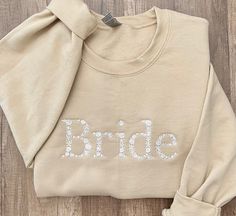 a bride sweatshirt with the word bride printed on it, sitting on a wooden floor