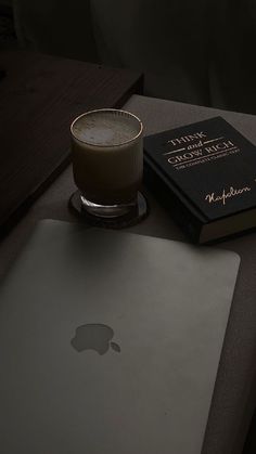 an apple laptop computer sitting on top of a table next to a book and drink