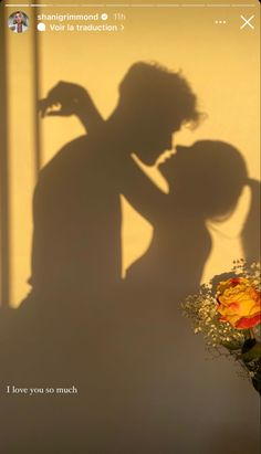 the shadow of a man and woman kissing next to a vase with flowers in it