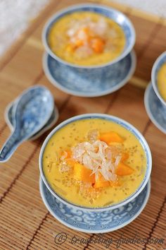 three bowls filled with soup on top of a bamboo mat and spoons next to it