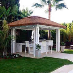 a white gazebo sitting in the middle of a lush green yard next to a palm tree