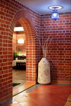 a large vase sitting in the middle of a room next to a brick wall with an arched doorway