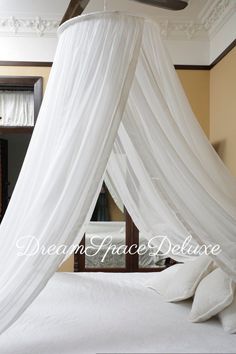 a canopy bed with white drapes and pillows