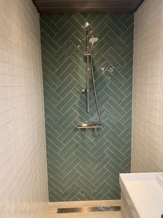 a bathroom with green herringbone tile on the shower wall