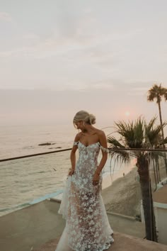 a woman standing on top of a cliff near the ocean wearing a dress with flowers