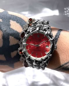 a wrist watch on someone's arm with red and silver jewels in the middle