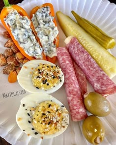 an assortment of meats and vegetables on a paper plate with pickles, olives