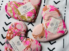 three pink and green heart shaped cushions on a black and white patterned cloth with labels