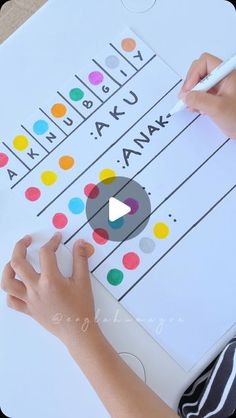 a person is writing on a white board with colorful dots and the word anak