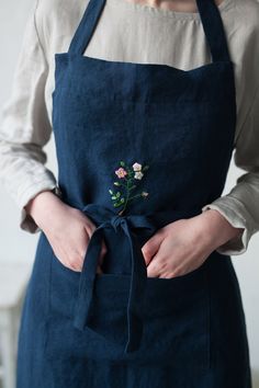 a woman is wearing an apron with flowers on the front and side, while holding her hands in her pockets