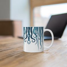 an octopus coffee mug sitting on top of a wooden table next to a laptop computer