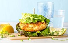 a chicken burger with lettuce and lemon wedges on a wooden cutting board