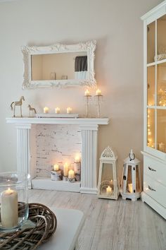 a living room filled with lots of white furniture and candles in front of a fireplace