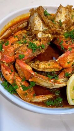 a white bowl filled with cooked crabs and garnished with parsley on top