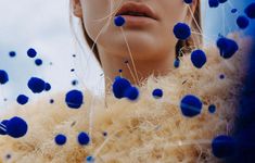 a woman with blue dots on her face and fur coat over her shoulders, looking at the camera