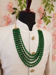 a green beaded necklace on a mannequin with pink flowers in the background