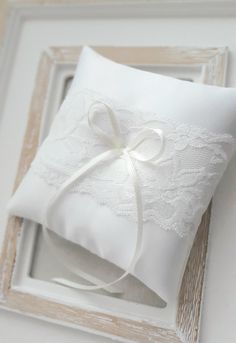 a white wedding ring pillow with a bow on the front and ribbon at the back