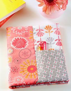 a pink and gray flowered notebook cover sitting on top of a table next to a vase with flowers