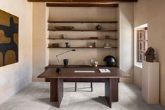 a wooden desk sitting under a window next to a shelf filled with vases and books