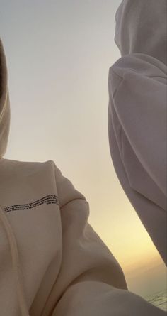 two women in white clothing standing next to each other with the sun setting behind them