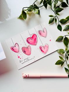 some pink hearts are on a white surface next to a pencil and green leaves, with a note that says happy valentine's day