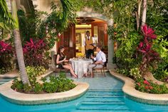 two people are sitting at a table in the middle of a small pool surrounded by greenery