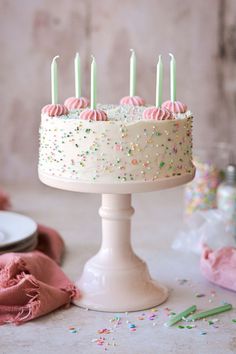 a white cake with pink frosting and sprinkles on it, surrounded by confetti