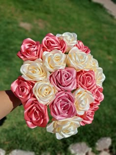 a person holding a bouquet of pink and white flowers in their hand with grass in the background